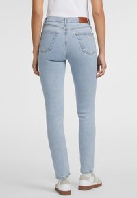 Ljusblå denim skinny jeans med hög midja, med bakfickor och ett brunt läderpatch på baksidan. Bärs med vita sneakers.