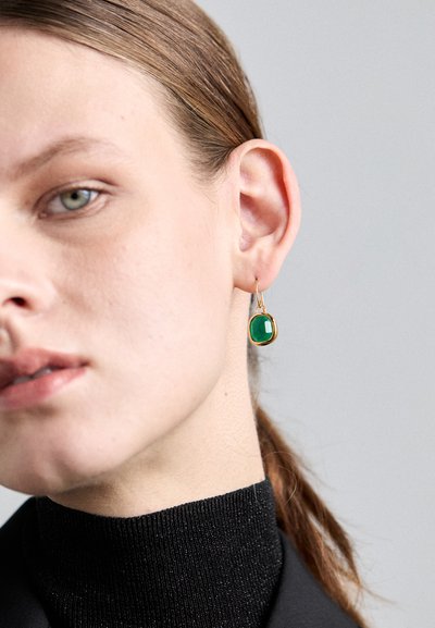 Boucles d'oreilles en or en forme de créoles avec une pierre verte ovale. La pierre est taillée et sertie dans un boîtier doré texturé.