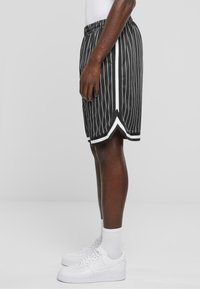 Shorts de sport rayés noir et blanc avec une taille élastique, caractérisés par un ourlet triangulaire et des accents blancs contrastants.