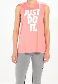 Top atletico senza maniche color corallo con grande scritta bianca "JUST DO IT." Abbinato a leggings grigi con un logo nero sul lato.