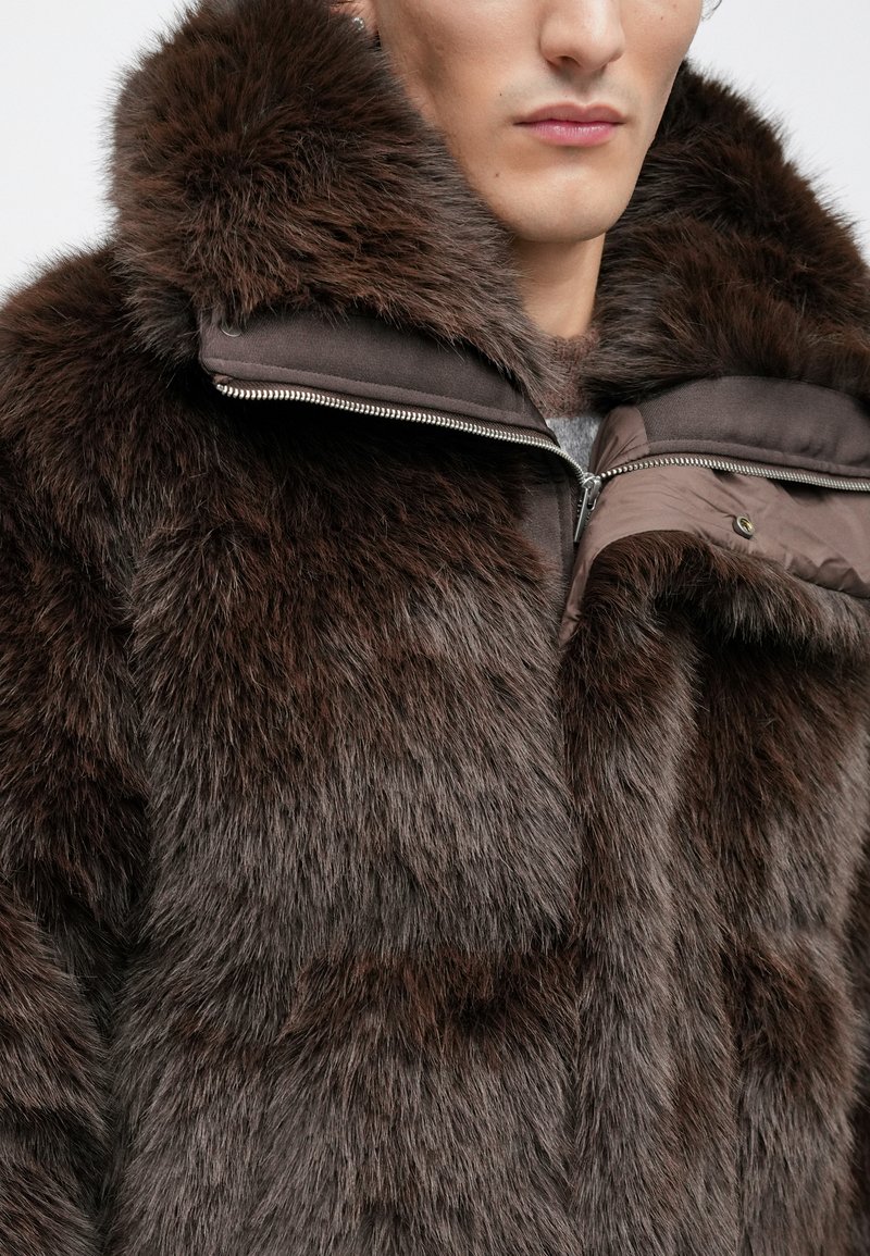 Brown faux fur coat with a plush texture, featuring a high collar, zippered closure, and contrasting brown lining.