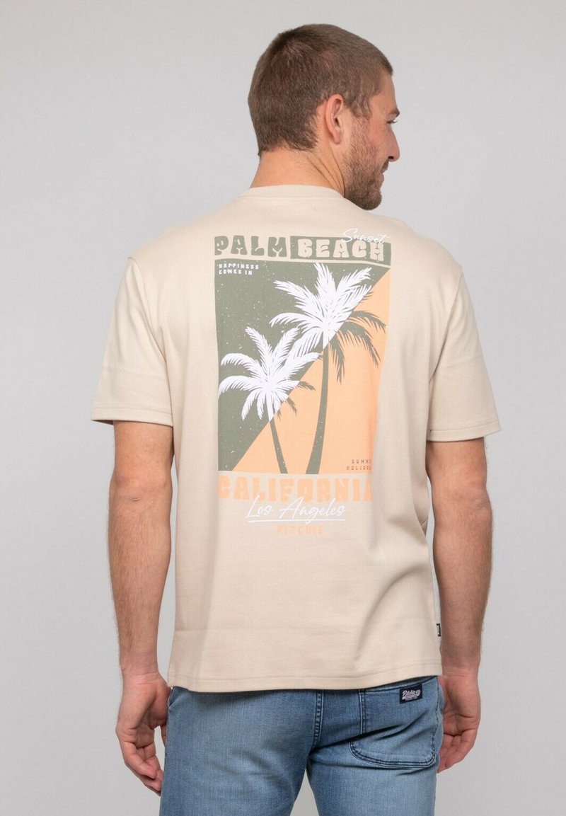 T-shirt beige en coton, avec un design imprimé comprenant des palmiers, des couleurs atténuées, et le texte "Palm Beach" et "California" au dos.