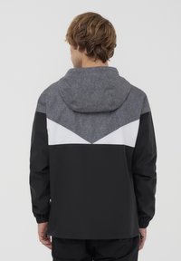 Giacca nera e grigia con cappuccio, caratterizzata da un pannello superiore grigio testurizzato, accento a chevron bianco e polsini elasticizzati.