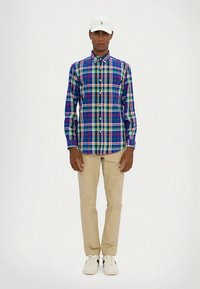 Pledas marškiniai mėlynos, žalios ir raudonos spalvų atspalvių; su sagomis apykaklė; ilgomis rankovėmis. Derinami su smėlio spalvos kelnėmis ir baltais sportbačiais.