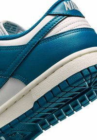 Zapatilla en tonos verde azulado y blanco con una parte superior de cuero suave, cuello acolchado y suela de goma texturizada con un patrón de banda distintivo.