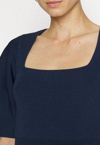 Námořnickomodrý rib rovný top s čtvercovým výstřihem, krátkými rukávy a texturovaným dolním panelem. Hladká látka s jemným leskem.