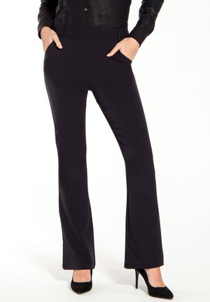 Zwarte stretchy uitlopende broek met een gladde textuur, voorzien van voorzakken en een hoge tailleband, gecombineerd met zwarte hoge hakken.