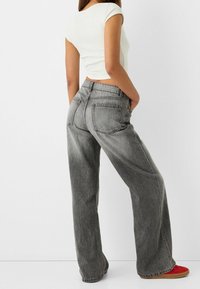 Grå jeans med hög midja och lös passform, med sidofickor, matchade med en croppad vit topp och röda skor. Texturerad denimfabric.