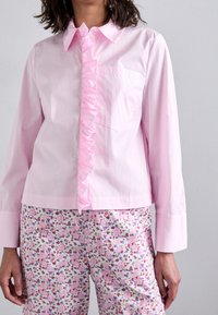 Pink button-up shirt with a ruffled front, long sleeves, and single chest pocket; paired with printed floral pajama pants.