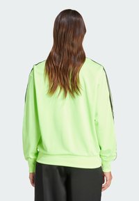 Neon-grüner Sweatshirt mit langen Ärmeln, ausgestattet mit schwarzen Seitenstreifen, weicher Textur und lässiger Passform. Minimalistisches Design.