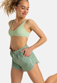 Crop top et shorts de sport vert menthe. Le soutien-gorge présente une texture côtelée; les shorts ont une taille élastique et un logo sur le côté. Tissu lisse.