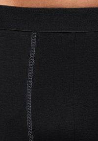 Schwarze dehnbare Stoffshorts mit breitem schwarzem Bund und subtilen kontrastierenden Nähten in der Mitte, die eine gerippte Textur zur Geltung bringen.