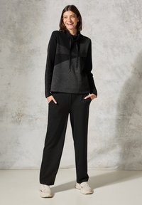 Felpa con cappuccio nera e grigia con un design triangolare e cordino. Abbinata a pantaloni neri larghi e sneaker chiare.