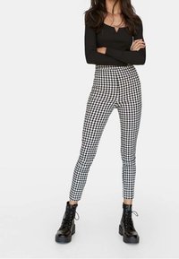 Zwart langemouwtop in combinatie met hoge taille, strakke zwart-wit geblokte broeken en stevige zwarte veterschoenen.