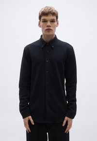 Tengerészkék, gombos ing texturált anyagból, hosszú ujjakkal és hegyes gallérral. Egyforma gombokkal és finom márkajelzéssel ellátva.