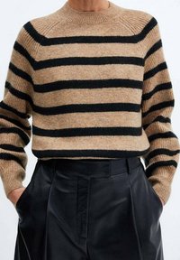 Pull en tricot beige avec des rayures noires, col et poignets côtelés. Associé à un pantalon noir taille haute, mettant en valeur une coupe décontractée.
