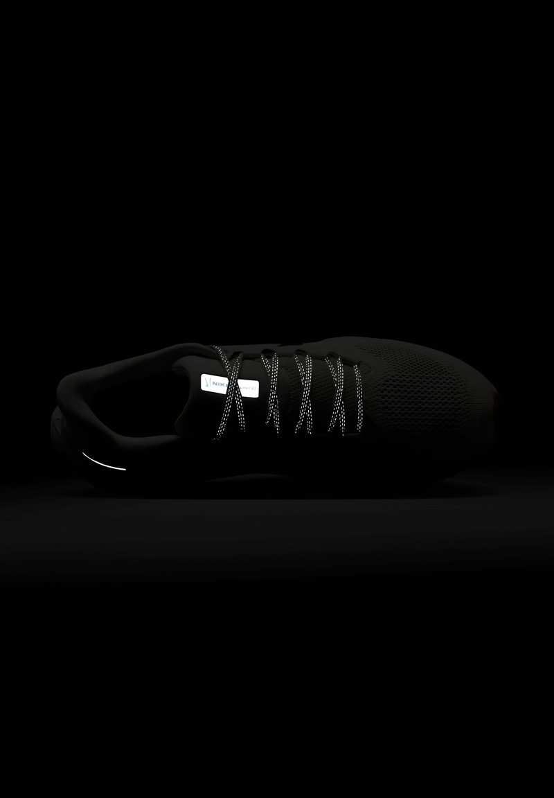 Scarpa sportiva nera con tomaia in mesh testurizzato, lacci riflettenti e un design elegante e minimalista. Presenta una punta arrotondata e un branding sottile.