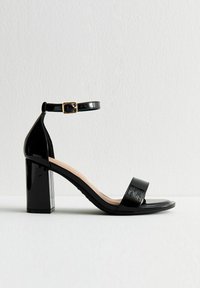 Czarne lakierowane sandały na wysokim obcasie z szerokim obcasem, pasek w okolicy kostki z złotymi akcentami oraz dwoma szerokimi paskami z przodu. Gładka tekstura.