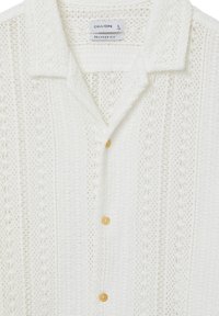 Chemise blanche à coupe décontractée avec un motif texturé, dotée d'un col et de boutons jaunes. Fabriquée en tissu léger et respirant.