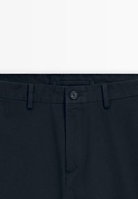 Pantalon noir avec passants pour ceinture, fermeture par bouton à la taille, et braguette à glissière cachée.