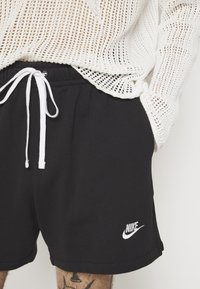 Svarta Nike-shorts med vit dragsko och logotyp. Mjuk tyg, elastisk midja. Bärs med en lös vit stickad tröja.