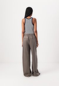 Paski top na ramiączkach w kolorze granatowym i białym, zestawiony z luźnymi, wysokim stanem oliwkowymi spodniami palazzo. Gładka tekstura materiału.