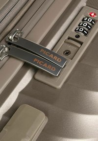 Valigia rigida beige con due cerniere argento etichettate "PICARD." Include una serratura approvata dalla TSA e un combinatore per la sicurezza.