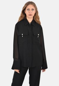 Camicia nera a maniche lunghe realizzata in tessuto leggero, con due tasche sul petto decorate con dettagli perlacei e colletto classico.