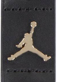 Black leather tag featuring a gold Jumpman logo. The logo depicts a silhouette of a person jumping and holding a basketball.