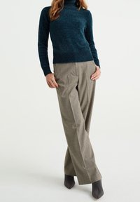 Teal polotröja med texturerad stickning; i kombination med högmidjade, rutiga vida byxor i en beige- och brunschemat.