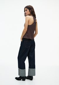 Brun rutigt linne med justerbara band, i kombination med lösa mörk denimjeans med grå manschett. Svarta klackboots fulländar outfiten.