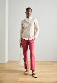 Cardigan en tricot beige avec des boutons sur une chemise blanche à col, associé à un pantalon tailleur rose et des chaussures plates beige. Sac à main crème.