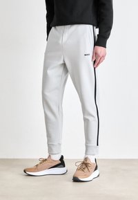 Light gray joggers with black side stripes and BOSS logo; elastic waistband and cuffs; paired with tan sports shoes featuring black accents.