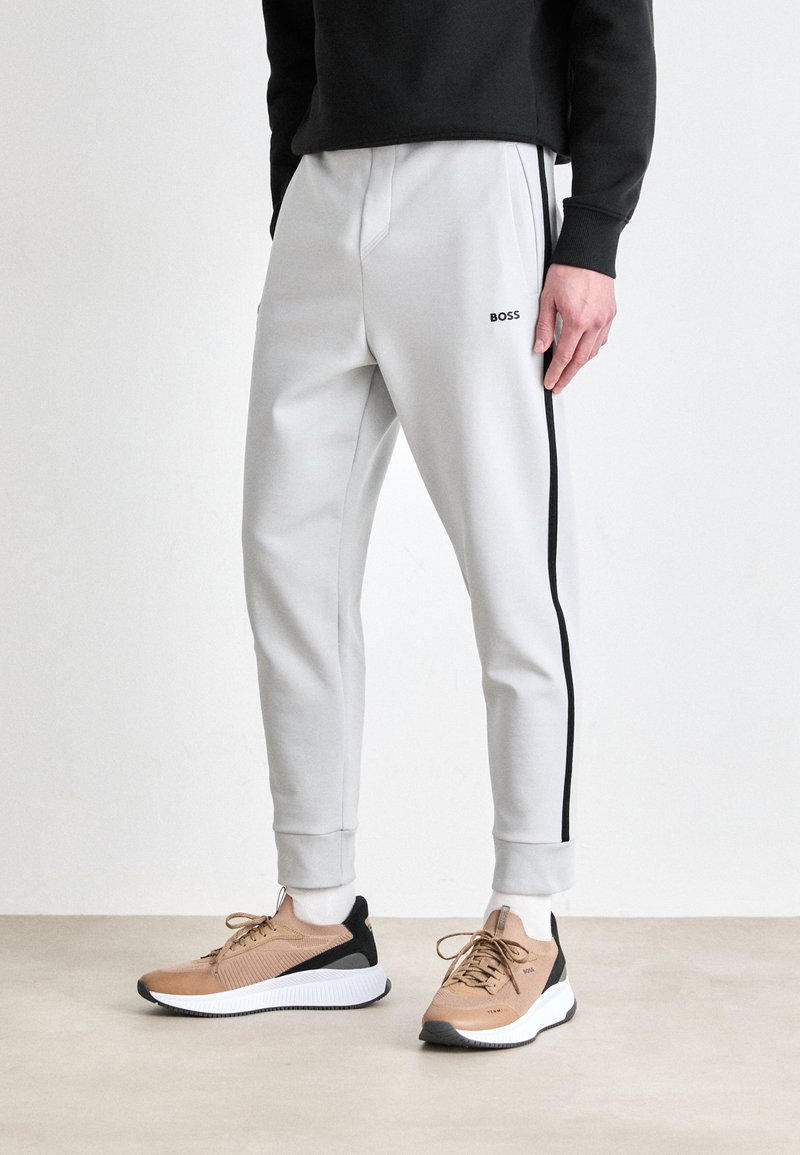 Light gray joggers with black side stripes and BOSS logo; elastic waistband and cuffs; paired with tan sports shoes featuring black accents.