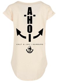 Beige T-Shirt mit kurzen Ärmeln, das ein großes schwarzes Grafikdesign mit "AHOI", Pfeilen und einem Matrosen-Logo auf der Rückseite zeigt. Angenehmer Baumwollstoff.