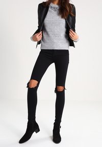 Svart läderjacka, grå tröja, trasiga svarta skinny jeans och ankelskor med låg klack. Texturerat tyg och slitna detaljer synliga.