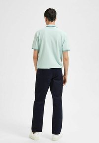 Light green polo shirt with short sleeves, blue trim, paired with dark navy pants and white sneakers. Visible shoulder seams and back details.