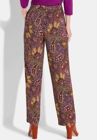 Frau trägt hochgeschnittene, weite Hosen mit buntem Paisley- und Blumenmuster, kombiniert mit braunen Ankle Boots mit Blockabsatz.