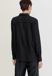 Black long-sleeve shirt with a collared neckline, a straight back yoke, and buttoned cuffs. Made of smooth fabric with a relaxed fit.