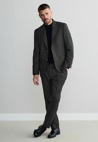 Gray pinstripe suit with a fitted design, featuring a single-button blazer and matching trousers. Black lace-up shoes with red accents.
