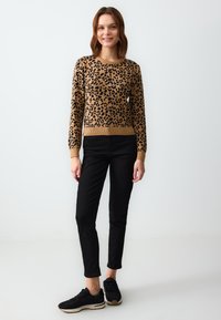 Sweter w panterkę w odcieniach brązu i czerni, z ribbrowanym dekoltem i mankietami. Połączony z czarnymi rurkami i czarnymi sneakersami.