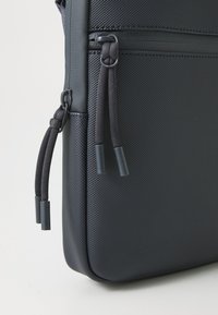 Schwarze, strukturierte Stofftasche mit einem Reißverschlussfach und geflochtenen Zugbändern. Verfügt über glatte Akzente und eine strukturierte, rechteckige Form.