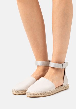 Espadrilles beige clair avec une semelle en jute tissé, un dessus en toile et une bride de cheville. Design à talon ouvert ; texture lisse et forme de pointe arrondie.