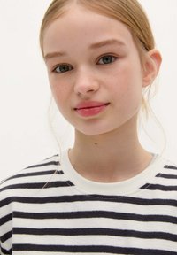 Koszulka bawełniana w paski, w granatowe i białe poziome pasy, okrągły dekolt, miękka tekstura, modelka o jasnej karnacji i blond włosach.
