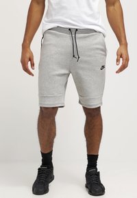 Gray cotton sweat shorts with an elastic waistband, drawstring, and side pockets; features a black Nike logo on the left thigh.