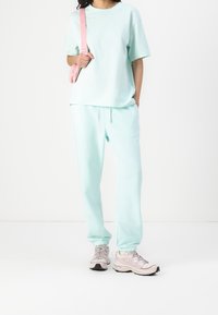 Luźny, miętowo-zielony strój codzienny z luźną koszulką i pasującymi spodniami z elastycznymi mankietami, zestawiony z jasnymi trampkami.