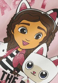 Sarjakuvamainen suunnittelu, jossa on hahmo, jolla on letitetyt hiukset, vaaleanpunainen kimalteleva takki ja raidoitettu paita, yhdessä valkoisen kissan kanssa, jossa on vaaleanpunaisia yksityiskohtia.