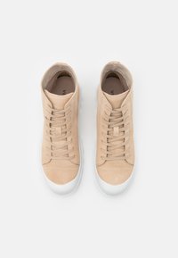 Sneaker alte beige in suede con una texture liscia, dotate di una suola in gomma bianca e lacci piatti. Logo visibile sulla soletta.