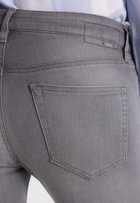 Jeans de mezclilla gris con una textura suave, que presentan un bolsillo trasero y detalles de costura sutiles. Exhibidos de lado, destacando el ajuste.