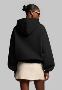 Black cropped hoodie with a large hood and wide sleeves, paired with a light beige mini skirt. Smooth texture, minimal detailing.